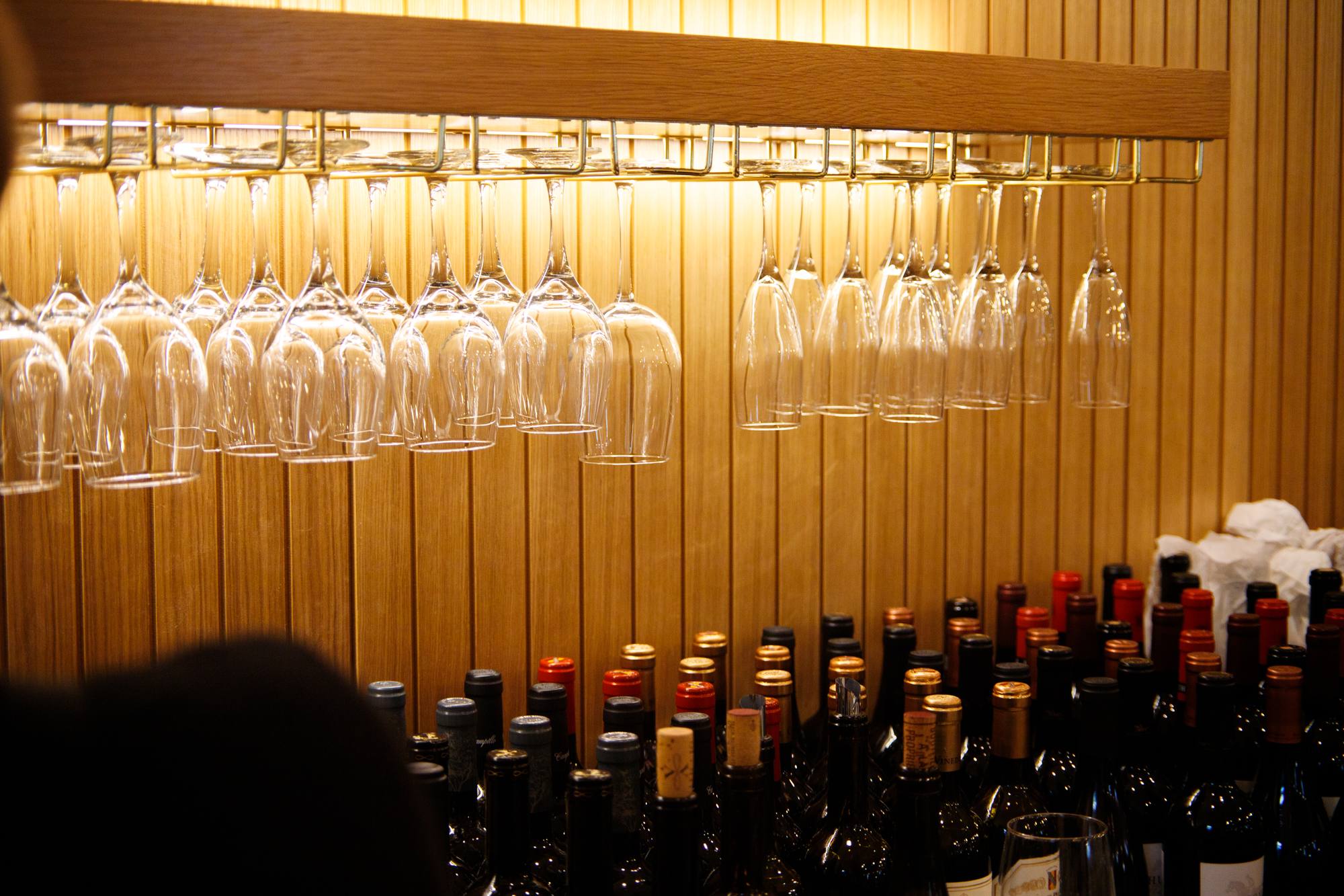 Wine glasses hanging above the lit wood-slat wine wall at Solera
