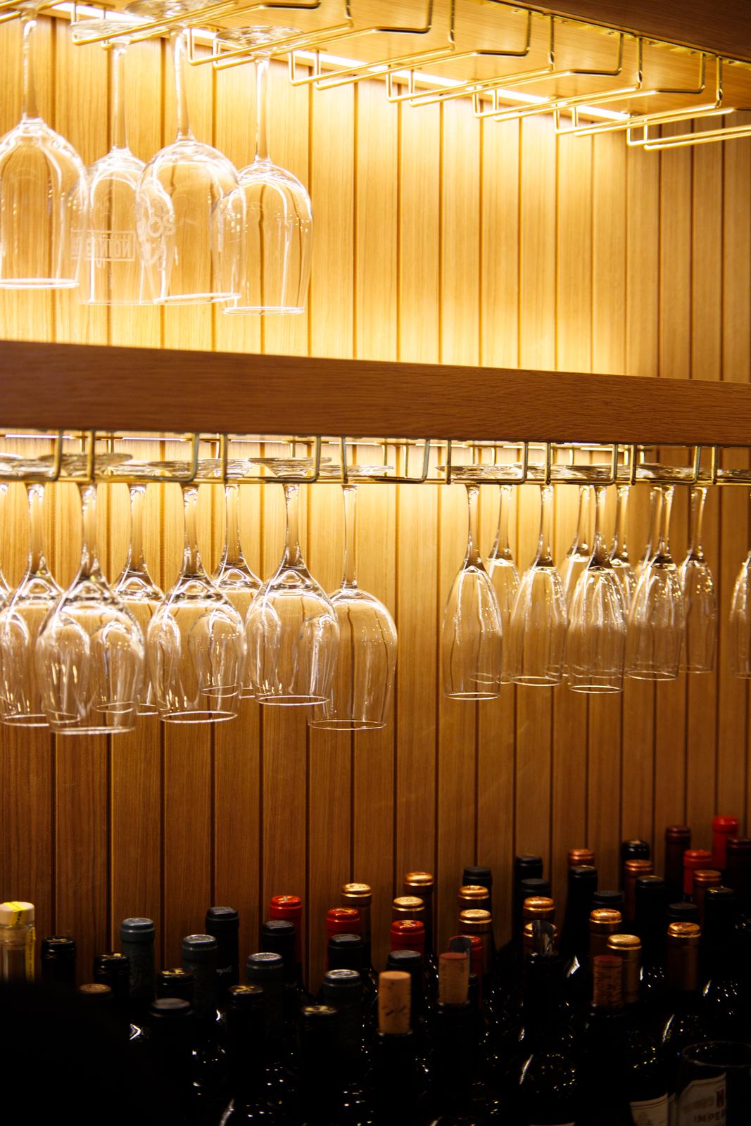Hanging stemware above rows of wine bottles on Solera's wood-slat wall